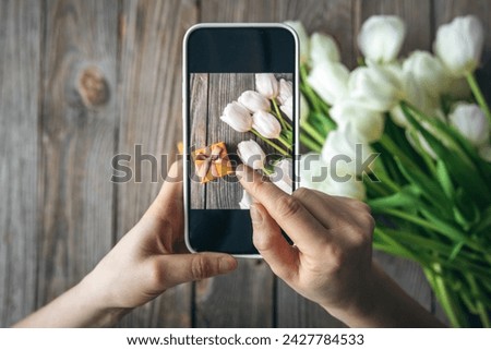 Woman take picture of bouquet of white tulips and gift box.