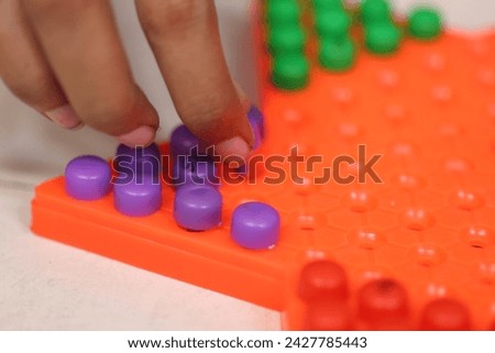 close up of fingers taking a peg from Chinese checkers board with all multi colour coins on board isolated in white backdrop