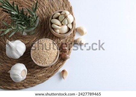 Dehydrated garlic granules in bowl, rosemary and fresh cloves on white table, flat lay. Space for text