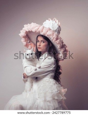 Conceptual photo of a girl or woman sitting with a white cat wearing a gorgeous dress and hat with a cake and burning candles on it. Birthday concept