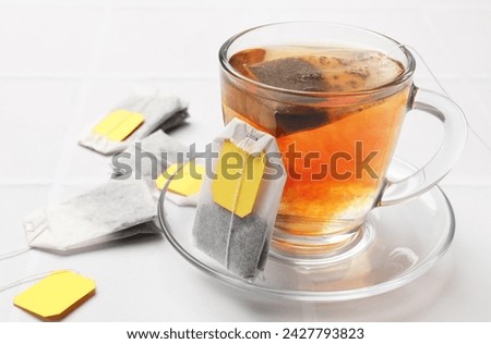 Tea bags and cup of aromatic drink on white table, closeup. Space for text Royalty-Free Stock Photo #2427793823
