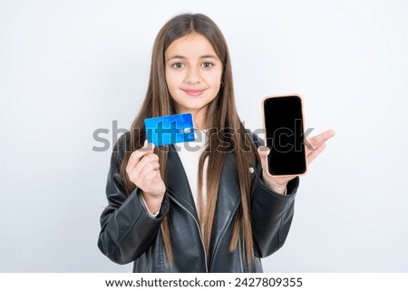 Photo of adorable Young beautiful teen girl wearing biker jacket holding credit card and Smartphone. Reserved for online purchases