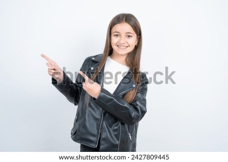 Optimistic Young beautiful teen girl wearing biker jacket points with both hands and  looking at empty space.