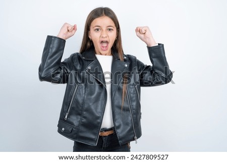 Shocked ecstatic Young beautiful teen girl wearing biker jacket win luck lottery raise hands up shout yea