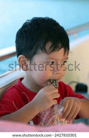 Exterior photo view portrait visual of a young eurasian asian handsome cute good looking kid child children male boy who is happy eating biscuits during outdoor activities on summer time sunny weather