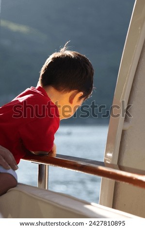 Exterior photo view portrait visual of a young handsome cute good looking kid child children male boy who is looking overboard on a boat or sail during outdoor boating on summer time sunny weather