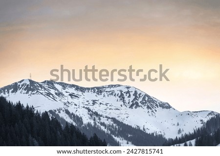 A serene view of a snow-capped mountain at sunset, embodying the concept of natural beauty and tranquility. The golden sky contrasts the dark, forested foothills, offering a moment of reflection