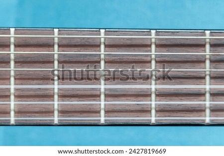 Close-up view of a guitar fretboard,  metal frets, strings against a blue background, object macro detail, extreme closeup, front view, frontal shot Classic acoustic guitar elements and parts up close Royalty-Free Stock Photo #2427819669