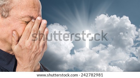 Elderly man with a face closed by hands on the background of the sky with a cross, a symbol of faith