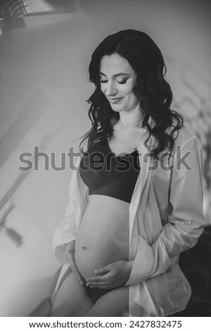 Belly of pregnant woman. Female waiting for newborn baby on white background. Young pregnant girl holding belly and caring about health. Pregnancy motherhood procreation concept. Black and white photo