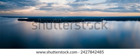 An aerial panoramic view of a large northern lake reflecting numerous shades of blue from the early morning clouds.
