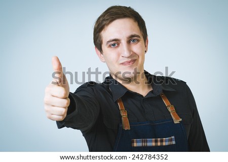 A shoot of young caucasian men in apron as a barmen. Showing the sign good, thumbs up.