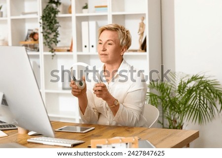 Mature female programmer with headphones working at table in office