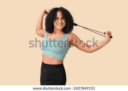 Sporty adult woman with fitness expander on beige background