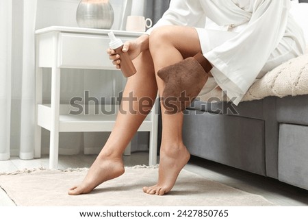 Self-tanning. Woman applying cosmetic product onto leg with tanning mitt on bed at home, closeup Royalty-Free Stock Photo #2427850765