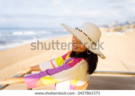 Gorgeous latina woman enjoys a bright summer day from the top of the lifeguard tower wearing a colorful dress and hat next to the beach