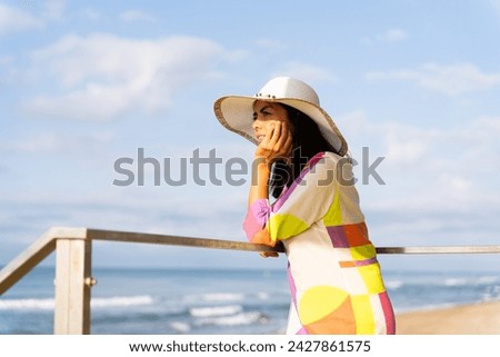 Pretty latina woman in a hat and colorful flashy dress relaxingly enjoying the views from a lifeguard tower on a beautiful summer day by the sea