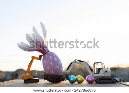 two small models of toy excavators, an eggshell with a large magnolia flower, multi-colored confetti eggs in backlight. Easter spring holiday concept, construction business greeting card