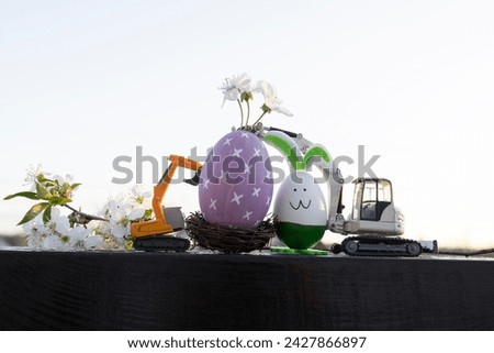 two models of toy excavators, eggshell with spring flowers, Easter bunny in backlight. Easter holiday concept for construction companies. postcard. soft focus