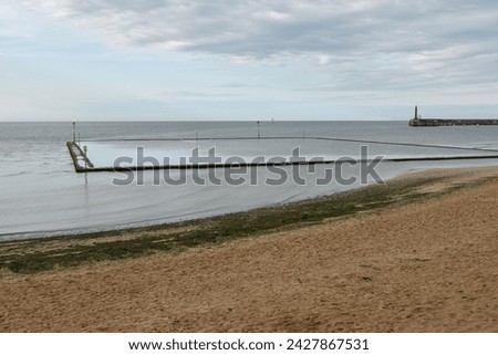 Outdoor Lido pool at Margate, Kent, UK with sand in the foreground.  The sea water filtering into the pool is calm at dusk with a sultry low light evening sky Royalty-Free Stock Photo #2427867531