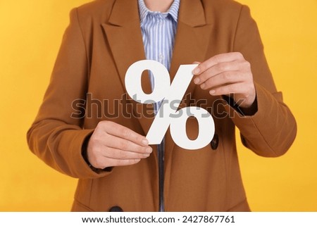Woman holding percent sign on orange background, closeup