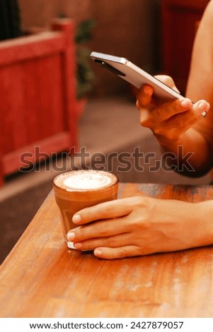 A woman takes a photo of a beautiful cappuccino on her smartphone. Stylish coffee shop concept. Young woman taking pictures of her latte for social media