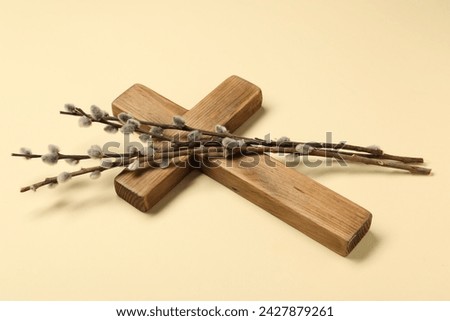 Wooden cross and willow branches on beige background. Easter attributes