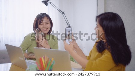 A woman holds a Chihuahua and smiles for a selfie taken by her friend in a bright cozy workspace