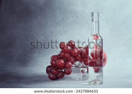 Water Bottle, Pomegranate and Red Grapes on Glass Stand, Textured Grey Background Royalty-Free Stock Photo #2427884633