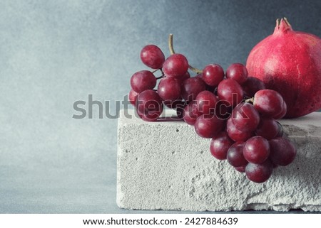 Red Grape Bunch and Whole Pomegranate on Textured Concrete Slab Royalty-Free Stock Photo #2427884639