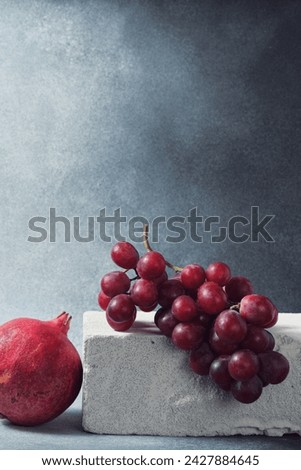 Red Grape Bunch and Whole Pomegranate on Textured Concrete Slab Royalty-Free Stock Photo #2427884645