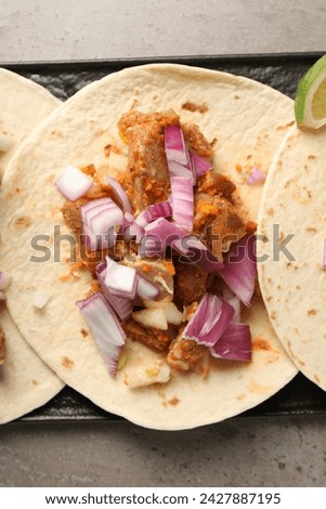 Delicious tacos with vegetables and meat on grey textured table, top view