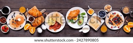 Breakfast or brunch table scene on a dark wood banner background. Top view. Assortment of sweet and savory food items. Royalty-Free Stock Photo #2427890805