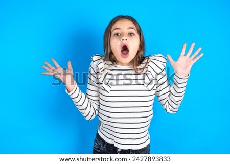 Surprised terrified Young kid girl wearing striped t-shirt Gestures with uncertainty, stares at camera, puzzled as doesn't know answer on tricky question, People, body language, emotions concept
