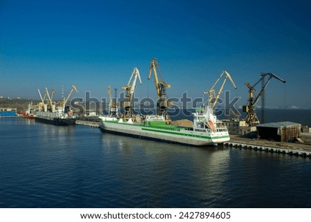 Cargo ship docking at seaport for transshipment. Cranes load containers for international trade. Maritime transport, global business, shipping industry, logistic operations, export in harbor. Royalty-Free Stock Photo #2427894605