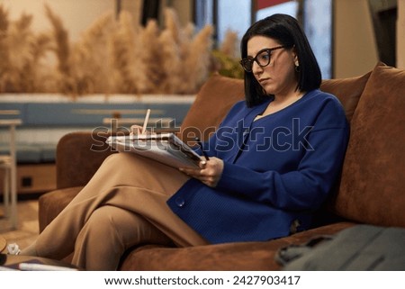 Side view portrait of Middle Eastern businesswoman writing in notebook while working in modern office or coworking area