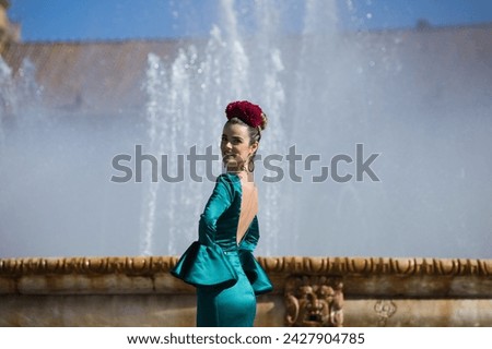 Beautiful young woman in a green frilly suit with a flower on her head. The woman is dancing flamenco and is in the most famous square in seville, spain, in front of its central fountain Royalty-Free Stock Photo #2427904785