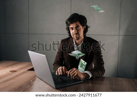 Portrait of happy successful businessman in suit working on laptop sitting at office desk, confident looking at camera, money rain on foreground. Finance and earning concept.