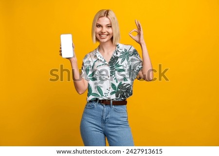 Photo of confident cheerful lady wear print shirt holding modern gadget empty space showing okey isolated yellow color background