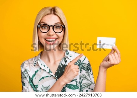 Photo portrait of attractive young woman point credit card excited dressed stylish leaves print clothes isolated on yellow color background
