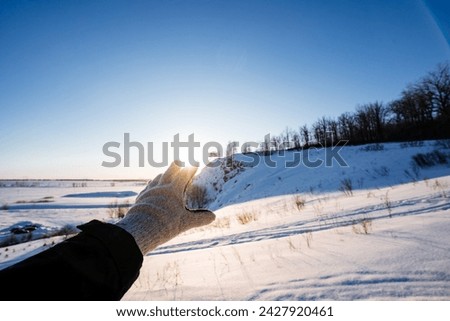 A gloved hand blocks the sunlight in winter, the glare of the setting sun shows through his fingers. Winter landscape, the beauty of Russia's nature. High quality photo