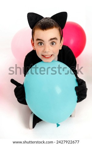 Emotional boy dressed as a black cat with a blue balloon. White background, Purim, Halloween