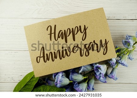 Happy Anniversary typography text on paper card decorate with flower on wooden background