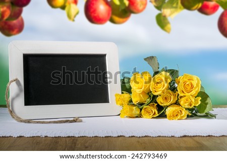 Image of a blank slate blackboard on a wooden table with yellow roses and apples in background