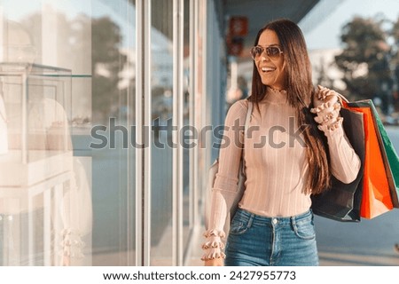 Beautiful woman wearing jeans and sunglasses, smiling and holding paper bags while shopping in the city center on a sunny warm day.