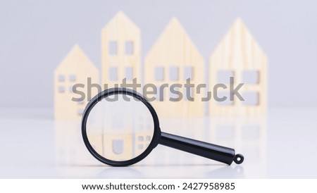 close-up magnifying glass on background of wooden houses on table. realtor services, finding a new house concept