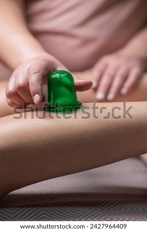 A massage therapist does a lymphatic drainage massage of the calf muscles with a vacuum plastic jar. Vertical photo.