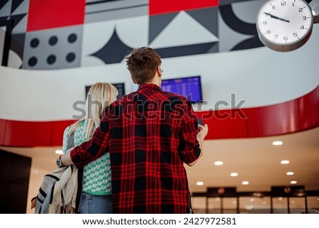 Back view of a young commuters standing at train station and looking at timetable. Rear view of passengers looking train schedule while standing at metro station and waiting for their train.Copy space Royalty-Free Stock Photo #2427972581