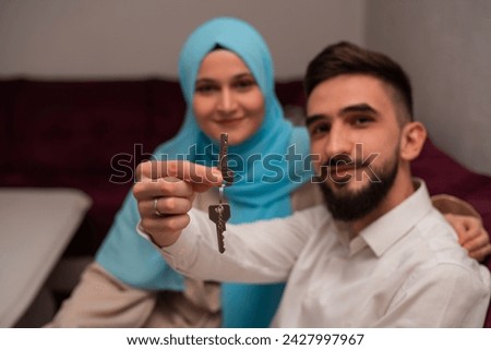 Happy Muslim Family Couple Showing New House Key To Camera Sitting On Sofa Indoors. High quality photo