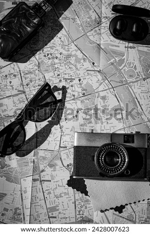 Black and white photo. Tourist kit: camera, wireless headphones, vape (electronic cigarette), sunglasses and city map. Millennials, travel and tourism, colorful adventures